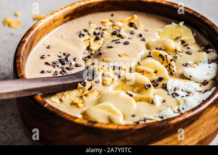 Chocolate smoothie bowl with coconut chips, banana and cocoa nibs in a wooden bowl. Healthy vegetarian breakfast concept. Stock Photo