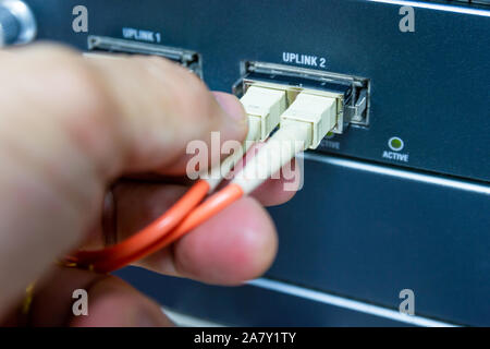 Technician connect fiber cable network to switch port in server room , Concept internet network management Stock Photo