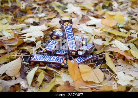 KHARKOV, UKRAINE - OCTOBER 17, 2019: Snickers chocolate bars in brown wrapping lies on autumn leaves background Stock Photo