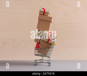 high pyramid of gift boxes in toy shopping cart on wooden background Stock Photo