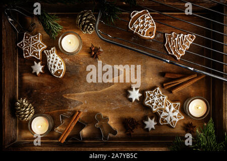 Gingerbread, burning candles and cookie cutters on a dark wooden tray, Christmas arrangement with copy space in the middle, flat lay, high angle view Stock Photo