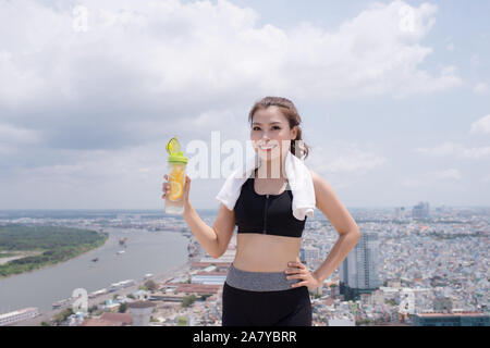 Technology and healthy lifestyle. Pretty young woman in sports wear holding bottle of water outdoors Stock Photo