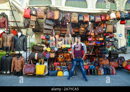 A foreign peddler in front of his stall of leather goods in St Lawrence Central Market square in the city center of Florence, Tuscany, Italy Stock Photo