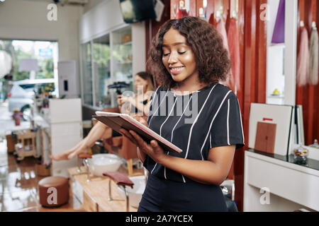Positive beauty salon manager checking booking application on digital tablet and reading feedback from clients Stock Photo