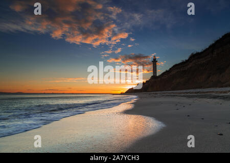 Sea lighthouse on the rocks at sunset Stock Photo