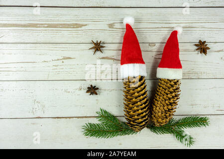 two santa hats on pine cones layout on white wooden background symbol of togetherness at christmas . Stock Photo