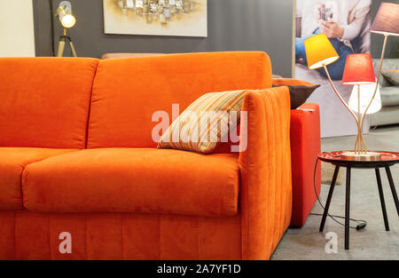 Bordeaux, France - June 1, 2019:Close-up of a beautiful orange sofa on which is placed a decorativ pillow and beside which is a design lamp placed on Stock Photo