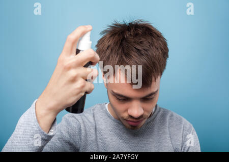 Portrait of young man in casual wear with head down, applying spray to his hair, treating premature hair loss or dandruff, healthcare and treatment. i Stock Photo