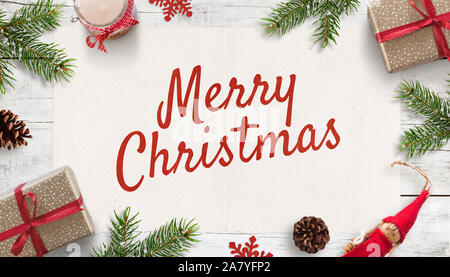 Merry Christmas text on white paper surrounded by Christmas decorations and gifts on white wooden surface. Top view, flat lay composition. Greeting ca Stock Photo