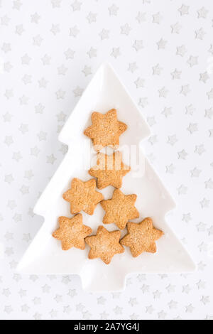 Star shaped homemade Christmas biscuits on tree shaped plate and silver star confetti on white background with copy space. Top view. Stock Photo