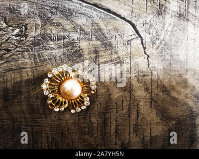 Brooch shaped like flower with big pearl in the middle for clothes isolated on wooden background. Stock Photo