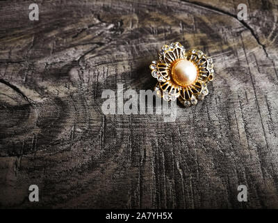 Brooch shaped like flower with big pearl in the middle for clothes isolated on wooden background. Stock Photo