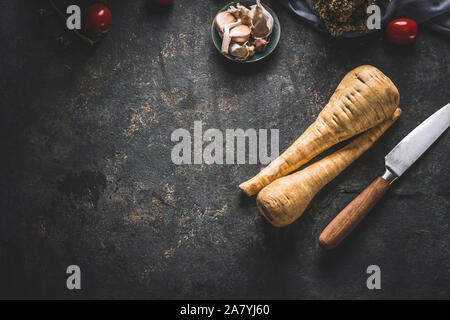 Food background with fresh parsnips roots on dark kitchen tables with knife. Top view. Vegetables cooking concept Stock Photo