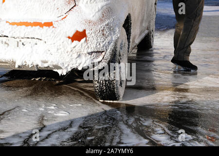 Car is cleaning with soap suds at self-service car wash. White soap suds on auto. Soapy water runs down. Stock Photo