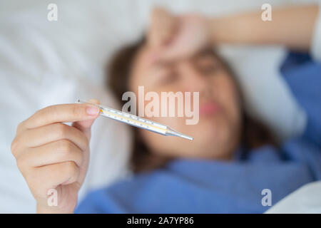 Asian Beautiful Woman Hypothermia has been measured by fever. Lie on the bed to give a body of rehabilitation. The concept of medical care to patients Stock Photo