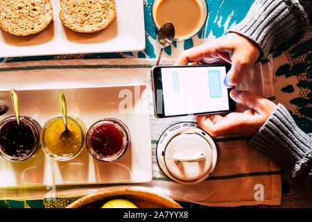 Above close up view of people doing healthy breakfast while answer messages on mobile phone -chat activity on device at home or hotel -  internet addi Stock Photo