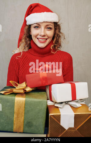 Portrait of young beautiful smiling woman posing with wrapped Christmas presents and looking at camera Stock Photo