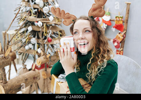 Excited young woman trying to guess what is inside of giftbox on Christmas eve Stock Photo