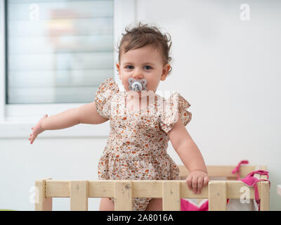 1 year old baby girl stands in her cot (or crib) Stock Photo