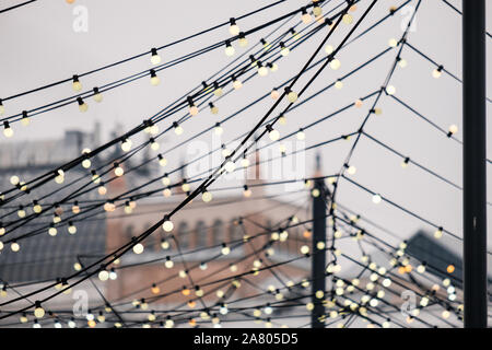 Web of wires of festive lighting with vintage light bulbs on the background of the cloudy sky in the evening. City street festive lighting. Stock Photo