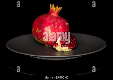 Group of one whole one piece of fresh red pomegranate on gray ceramic plate isolated on black glass Stock Photo