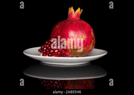 Group of one whole one piece of fresh red pomegranate on white ceramic plate isolated on black glass Stock Photo
