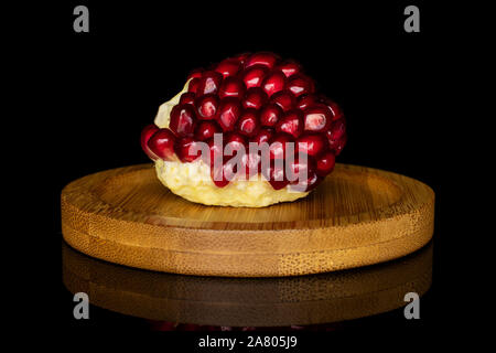 One piece of fresh red pomegranate on bamboo coaster isolated on black glass Stock Photo