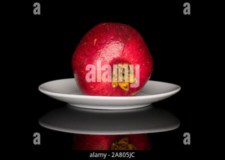 One whole fresh red pomegranate on white ceramic plate isolated on black glass Stock Photo