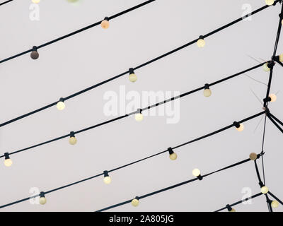 Web of wires of festive lighting with vintage light bulbs on the background of the cloudy sky in the evening. City street festive lighting. Stock Photo