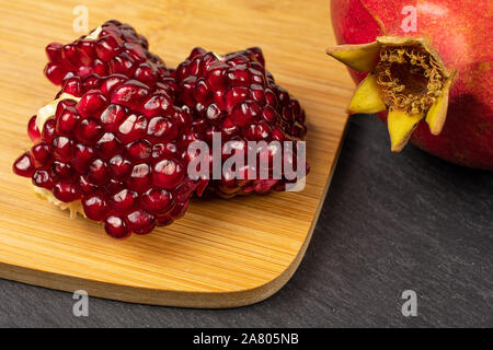 Group of one whole three pieces of fresh red pomegranate on bamboo cutting board on grey stone Stock Photo
