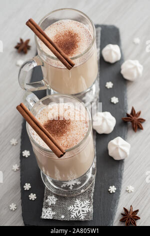 Eggnog in glass cups with a delicate foam, spices and a cinnamon stick Stock Photo