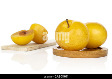 Group of two whole two halves of fresh yellow plum on round bamboo coaster on wooden cutting board isolated on white background Stock Photo