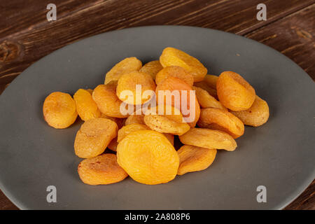 Lot of whole dried orange apricot on gray ceramic plate on brown wood Stock Photo