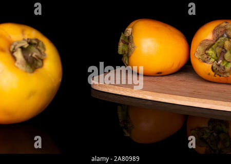 Group of three whole sweet orange persimmon on bamboo cutting board isolated on black glass Stock Photo