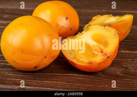 Group of two whole two halves of sweet orange persimmon on brown wood Stock Photo