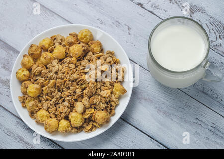 White plate of granola with glass of milk on grey wooden boards. A mixture of cereals dried and nuts with milk at breakfast. Glass cup of milk with ro Stock Photo