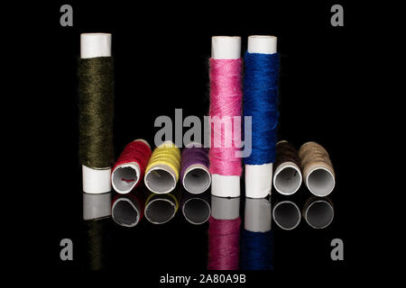 Group of eight whole colorful sewing thread spool upright isolated on black glass Stock Photo