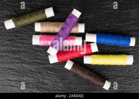 Group of eight whole sewing thread spool flatlay on grey stone Stock Photo