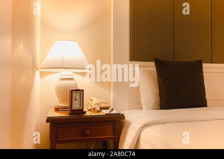 Hotel bedroom with reading lamp and clock with telephone in modern hotel. Stock Photo