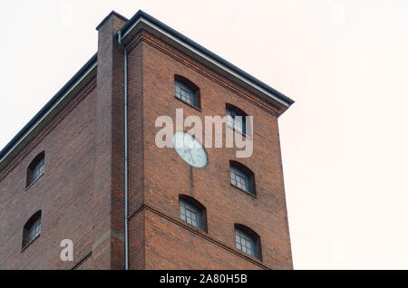 Exterior of a commercial red brick building or industrial factory with clock on the wall viewed low angle Stock Photo