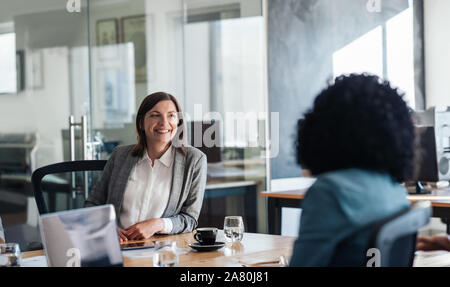Two smiling businesswoman talking together around an office table Stock Photo