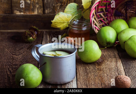 Rural mug with apple tea hot drink and fresh green apples,  hygge autumn or winter beverage on rustic wooden table Stock Photo