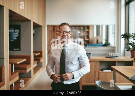 Mature businessman smiling confidently while standing alone in the cafeteria of a bright moderrn office Stock Photo