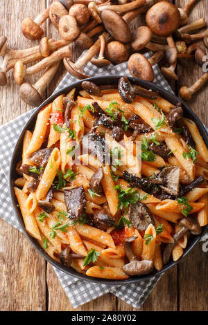 Italian penne pasta with Armillaria mellea mushrooms, tomatoes, cheese and parsley close-up in a plate on the table. Vertical top view from above Stock Photo