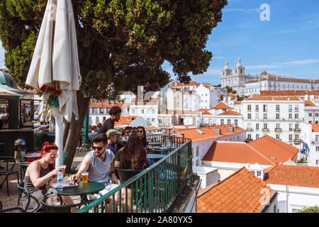 Lisbon, Portugal : Young people relax at an outdoors kiosk cafe at the Miradouro das Portas do Sol viewpoint. Alfama old town and Monastery of São Vic Stock Photo