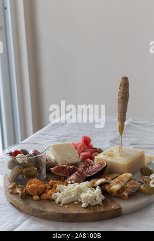 Mediterranean cheese plate with figes and olives placed on a round half marble half wooden cheese board. Vertical composition. Copy space. Stock Photo
