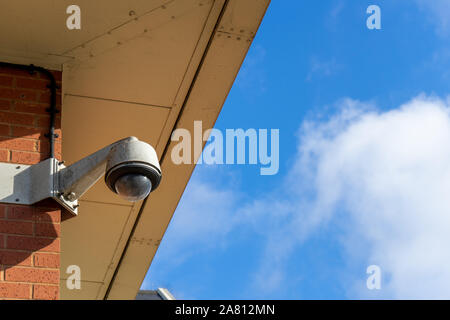 A security camera on a wall with blue sky in the background Stock Photo