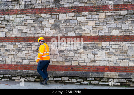 a builder or construction worker wearing high visibility clothing and a hard hat walking Stock Photo