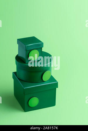 Christmas gift boxes, in a stack on a green background. Xmas gifting themed. Christmas presents with round empty tags. Pile of diverse shaped gifts. Stock Photo