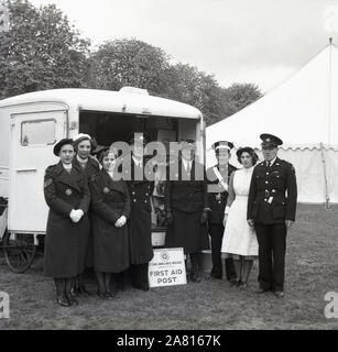 1950s, historical, members of the St John Ambulance Brigade (Cambridge Division) standing in their uniforms outside a First Aid Post at a tented exhibition, England, UK. Dating back to 11th century Jerusalem and the first knights of St John, in England, the St John Ambulance Association was founded in 1877 to teach industrial workers first aid. in 1887, the St John Ambulance Brigade was founded which saw trained uniformed volunteers provide a first aid and ambulance service at public events. In 1968, the Brigade and the Association merged to form a unifed St John Ambulance. Stock Photo